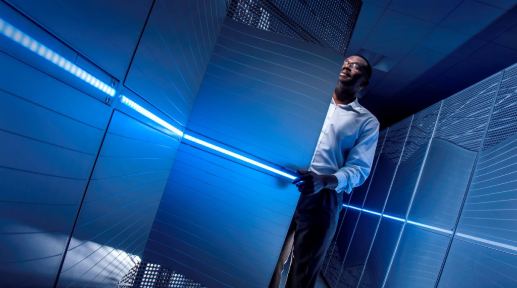 A man opens a door to a supercomputer rack. The computer is illuminated in blue light.