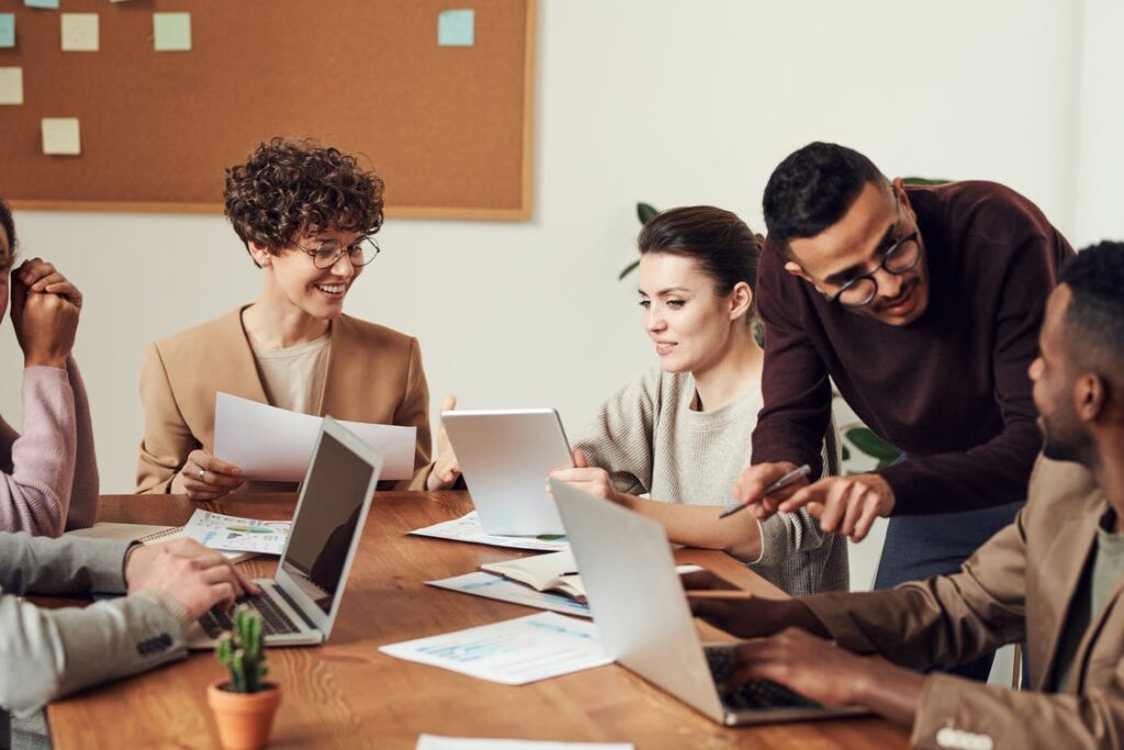 A group of employees sit with laptops around a meeting table.