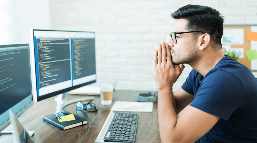 A man sits looking thoughtfully at a computer screen with his hands under his chin.