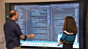 A man and a woman looking at some code on a large screen