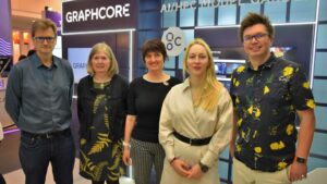 A group of two men and three women stand in front of the Graphcore exhibition stand at a conference.