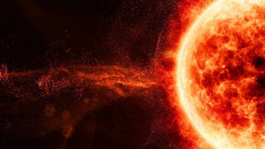 A photograph of a solar flare, large red and orange fireball on a dark bakground