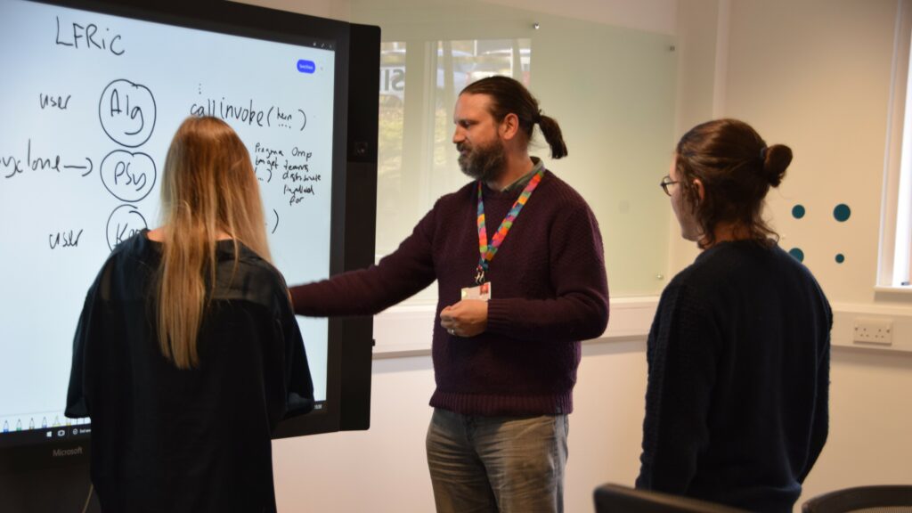 Three people standing around a digital whiteboard during a training session