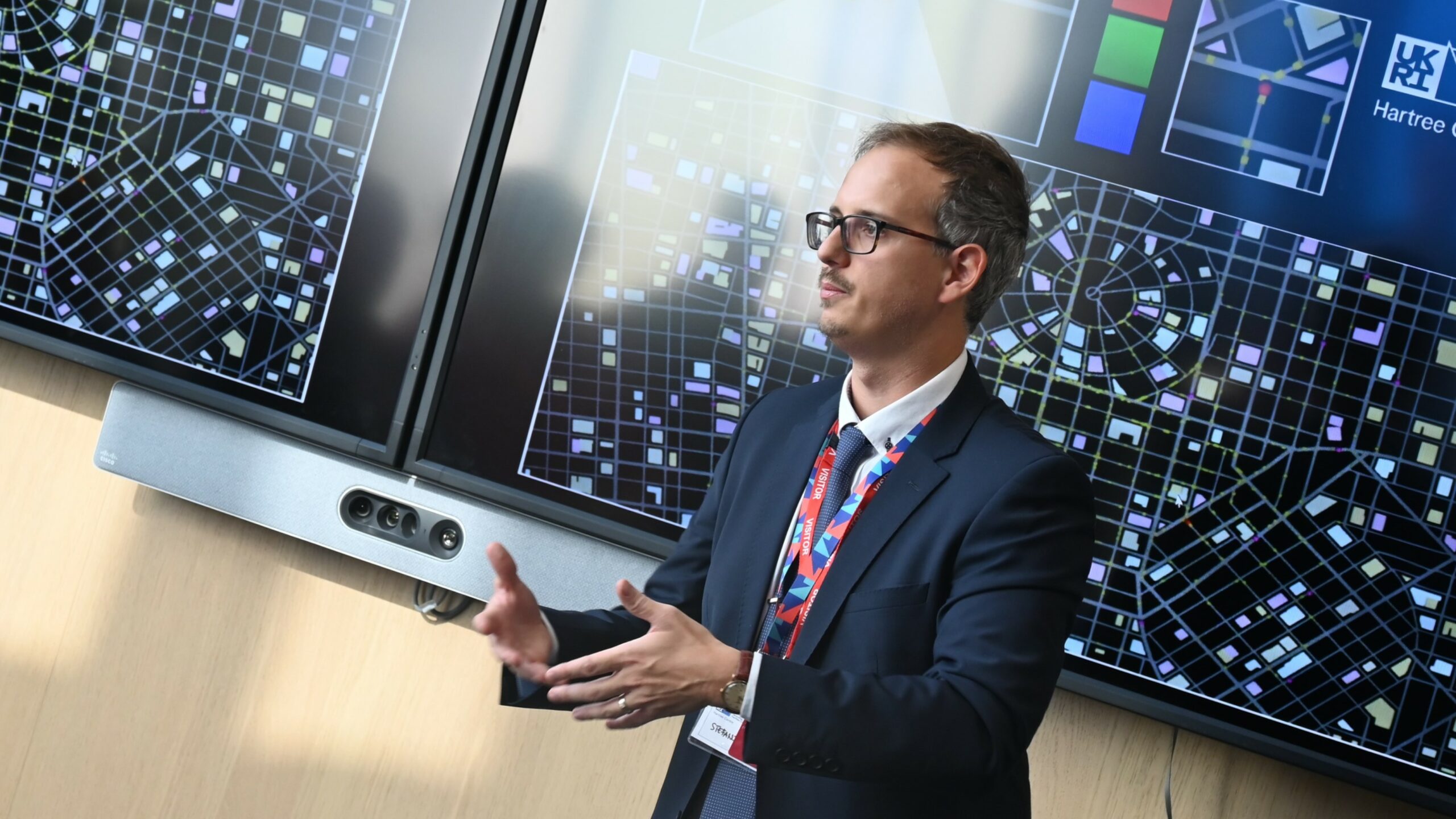A man speaking in front of a quantum computing visualisation on a screen.