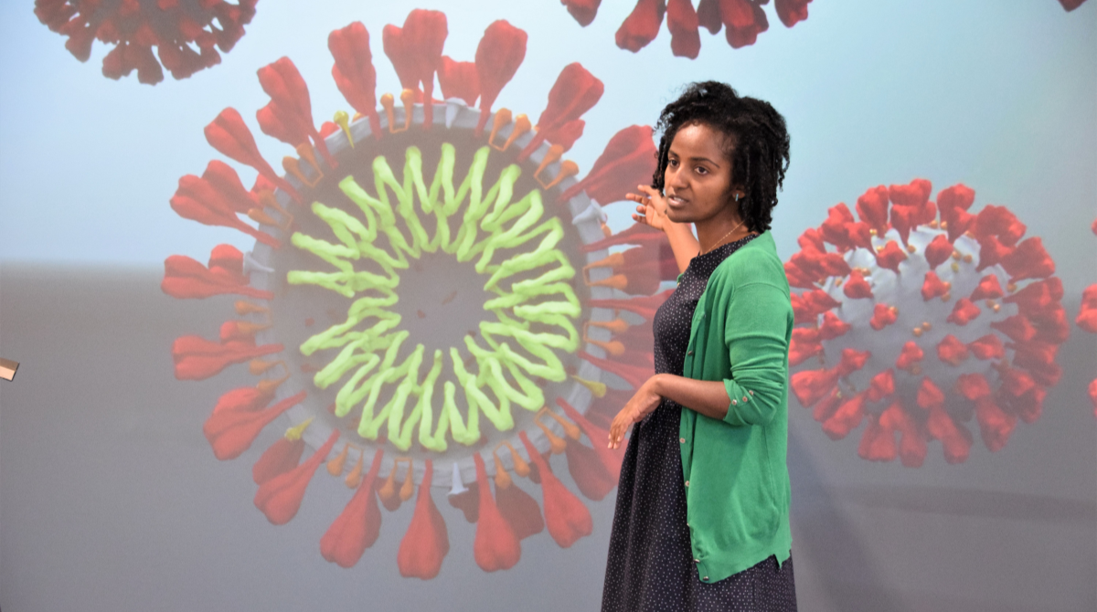 A woman pointing as a visualisation screen showing a virus molecule.