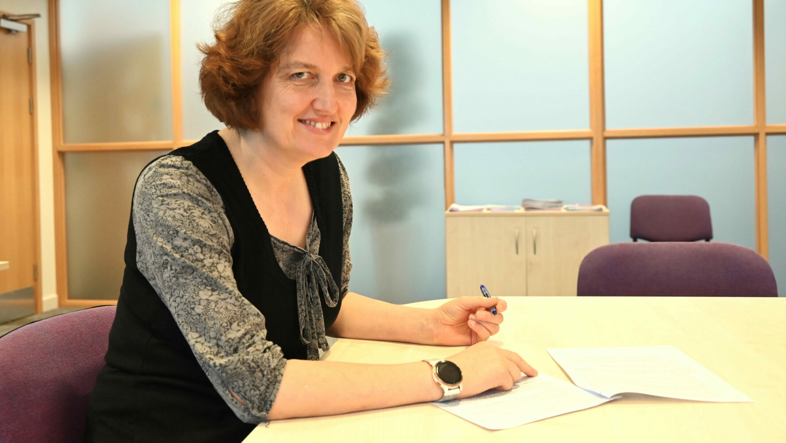 Hartree Centre Director Kate Royse signs the collaboration agreement for the Digital and AI Skills Network, sitting at a desk and smiling into the camera.